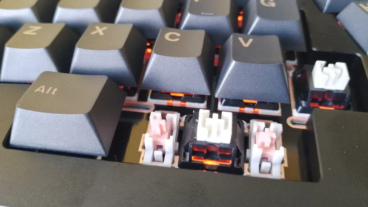 Zbliżenie na odkryte przełączniki mechaniczne i gniazda hot-swap w klawiaturze Epomaker Tide Alice, widoczne po zdjęciu niektórych keycapów.