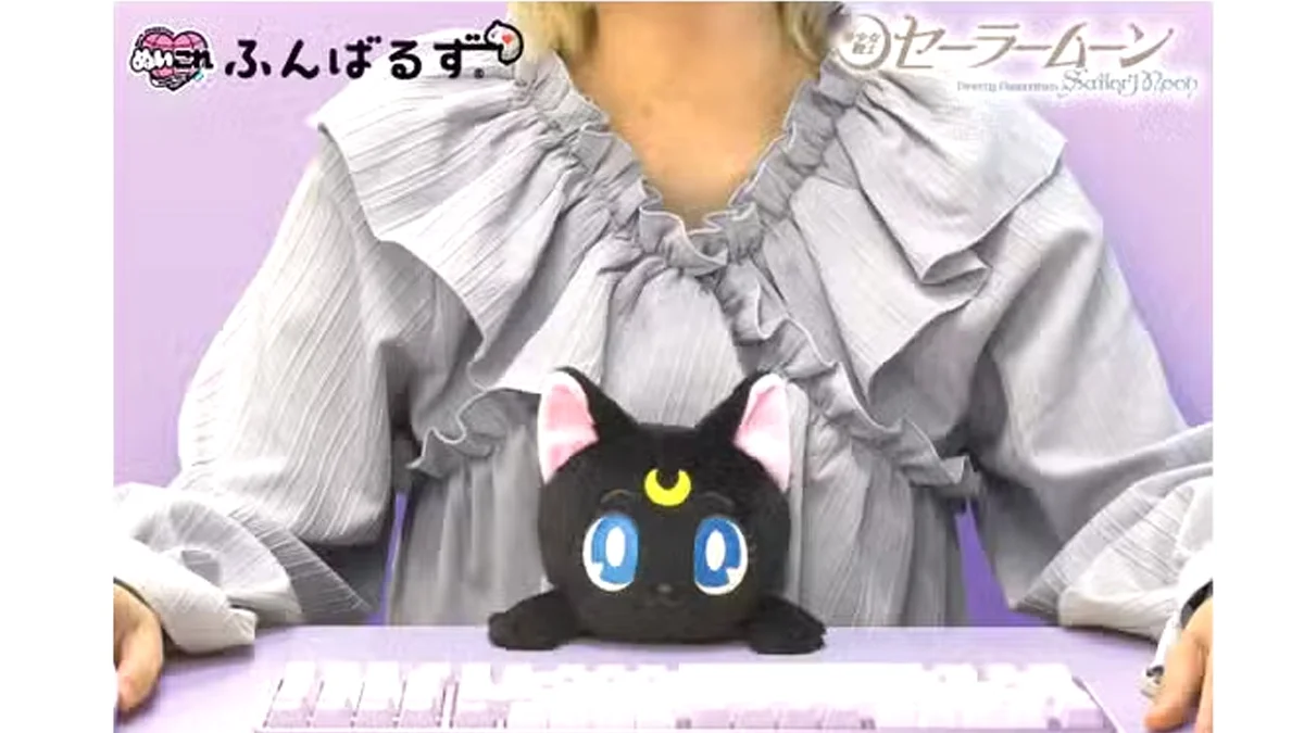 Czarna pluszowa Luna z Sailor Moon oparta o krawędź biurka, pomagająca utrzymać prawidłową postawę ciała podczas pracy przed komputerem.